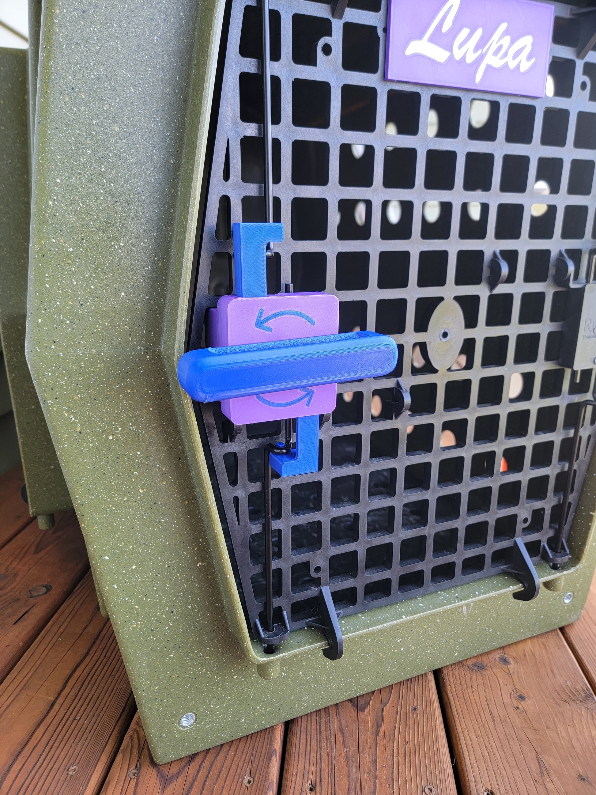 Close-up of blue and purple Ruffland kennel door lever with directional arrow, viewed from outside kennel